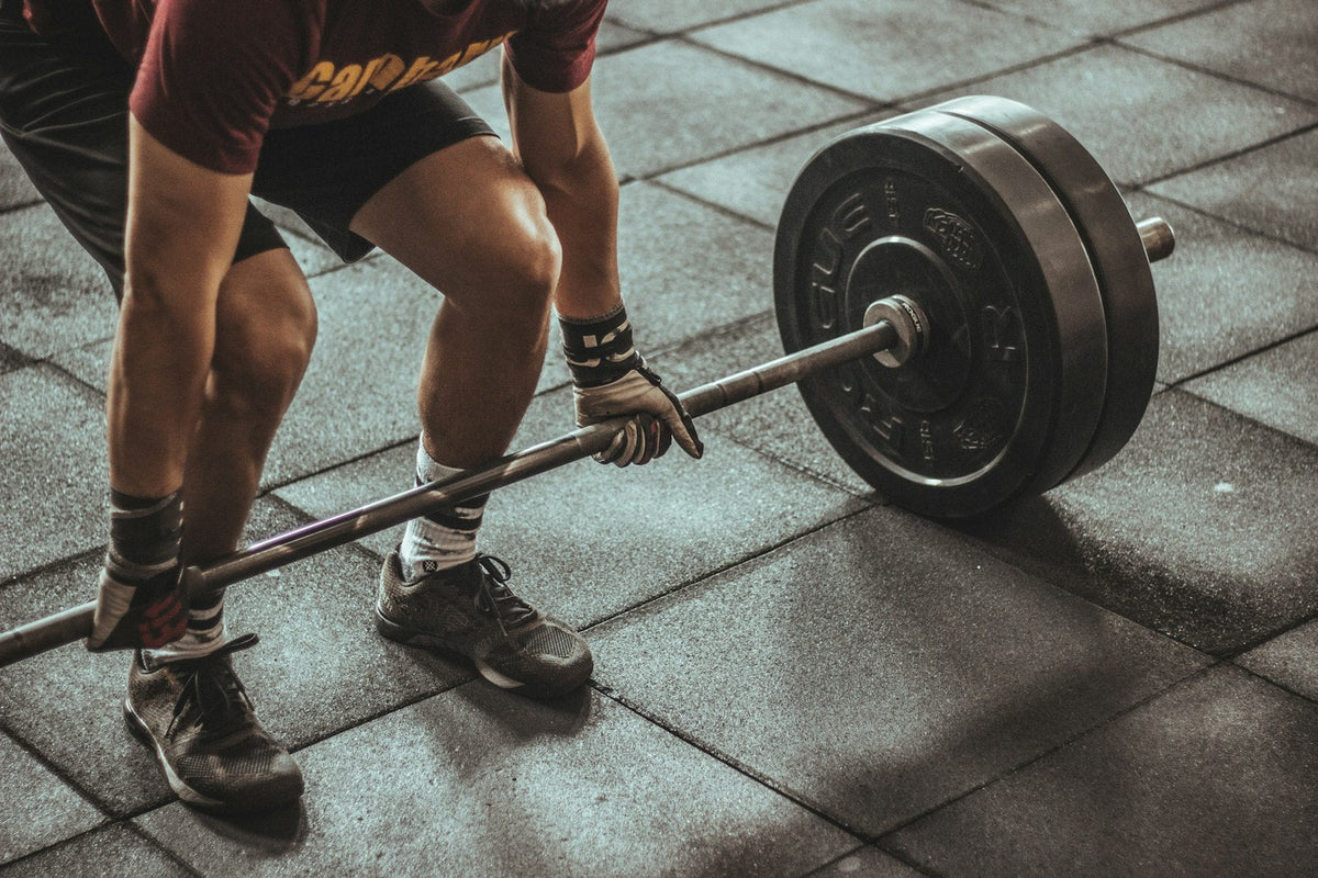 Homme qui soulève une lourde barre de musculation depuis le sol d'une salle de sport