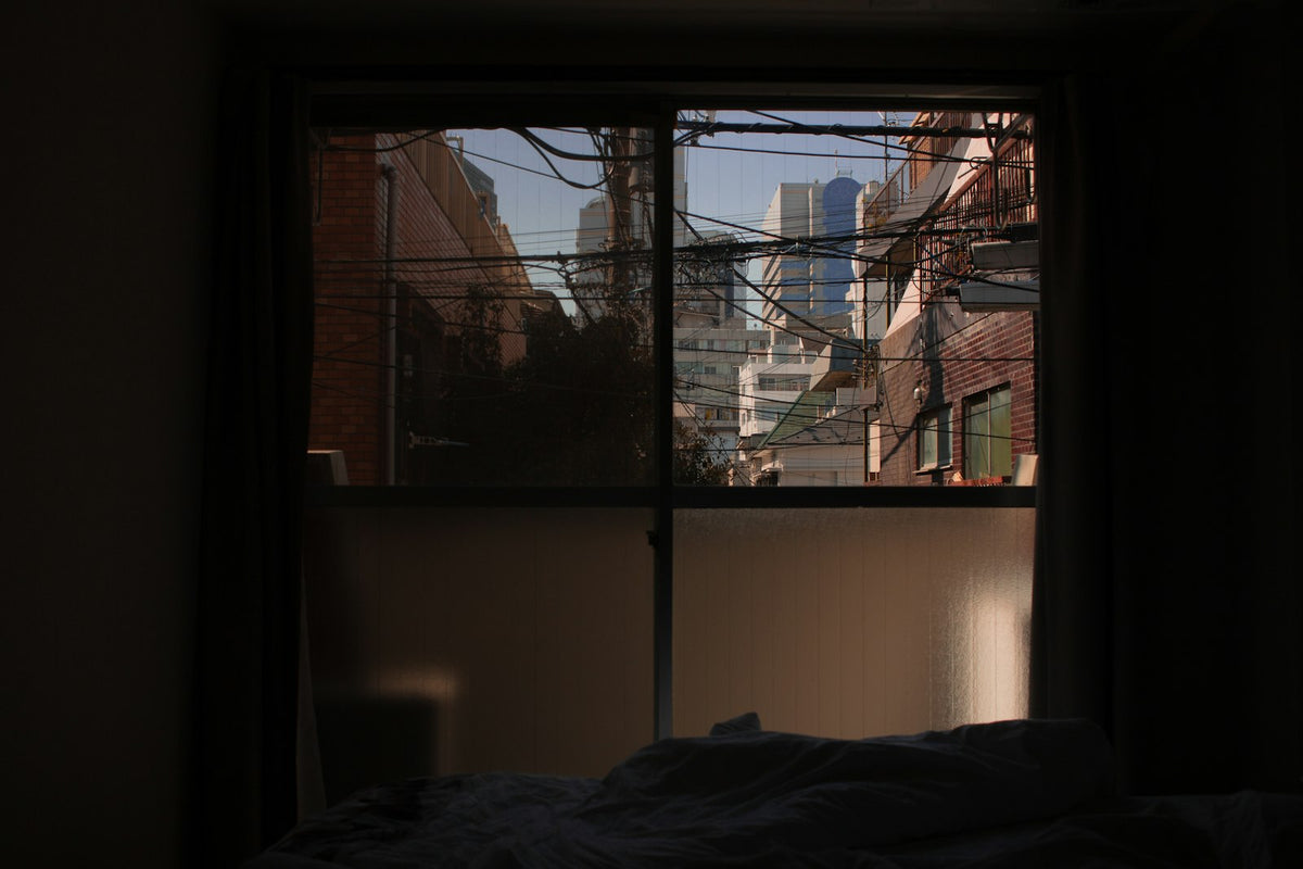 Chambre sombre avec un lit face à une fenêtre donnant sur la ville